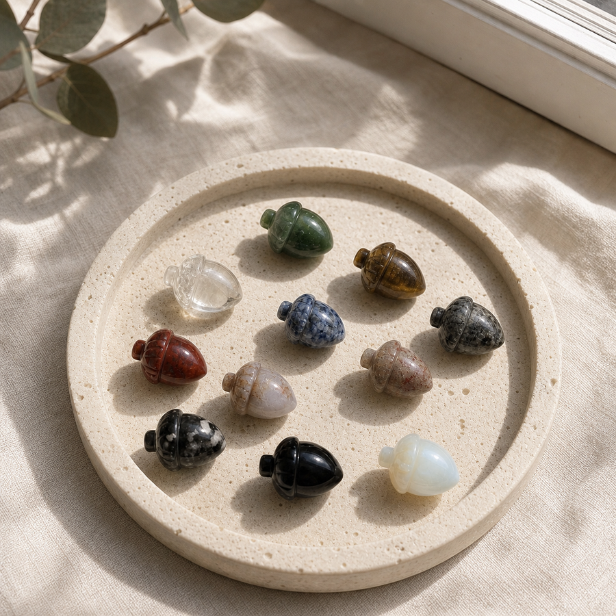 Assorted polished crystal acorn carvings arranged on a cream stone plate in natural window light