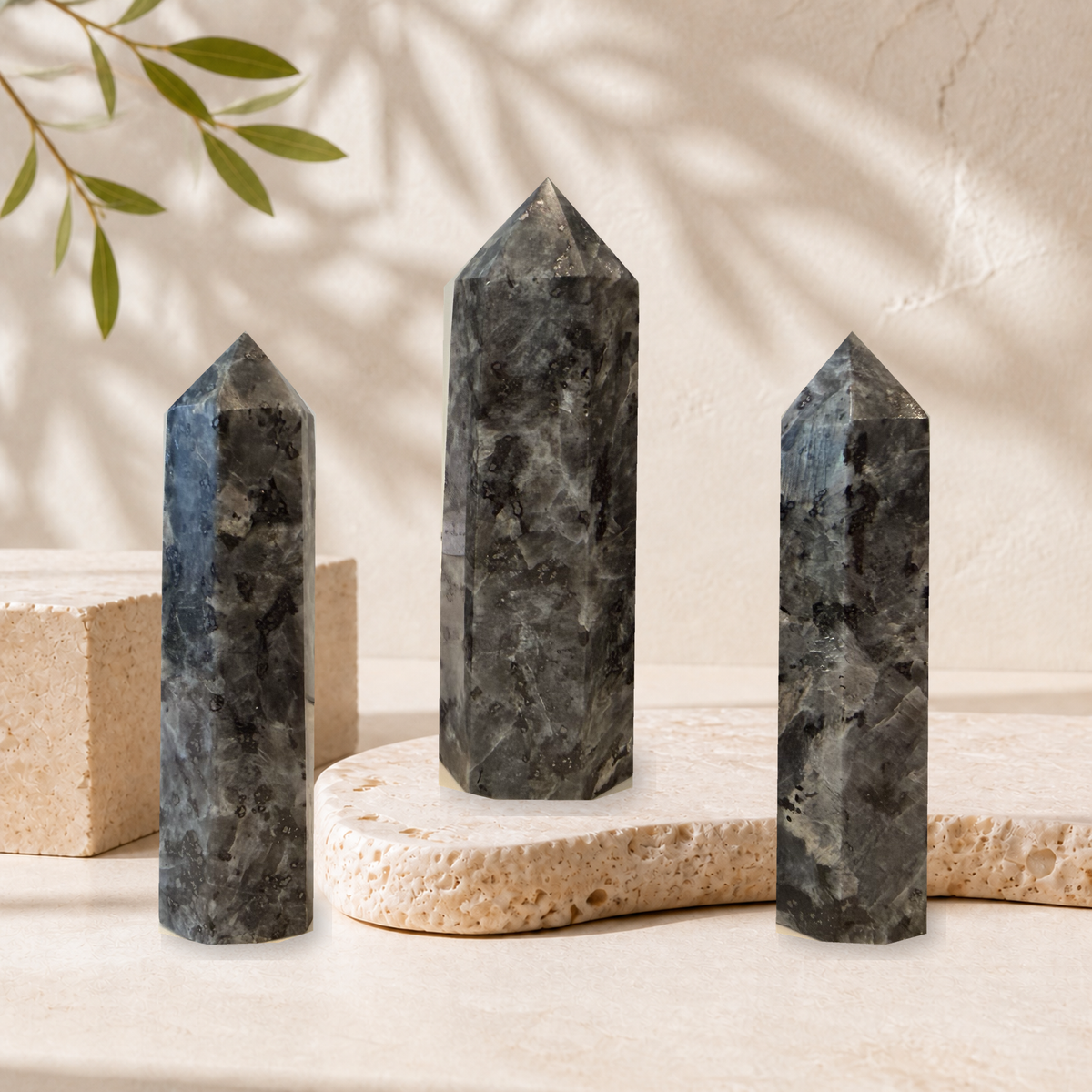 Three polished Larvikite towers displayed on cream stone slabs
