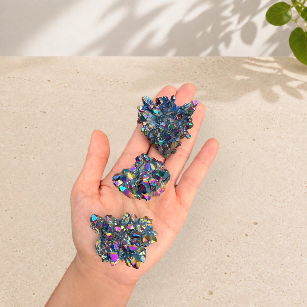 Three rainbow aura quartz clusters resting in an open palm to show their approximate size.