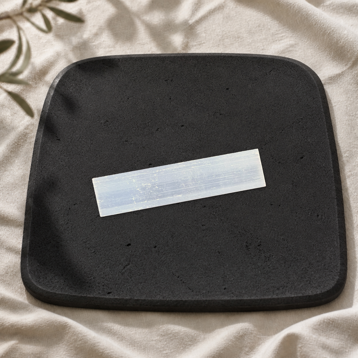 Medium satin spar gypsum wand showing its natural fibrous texture on a black limestone plate.