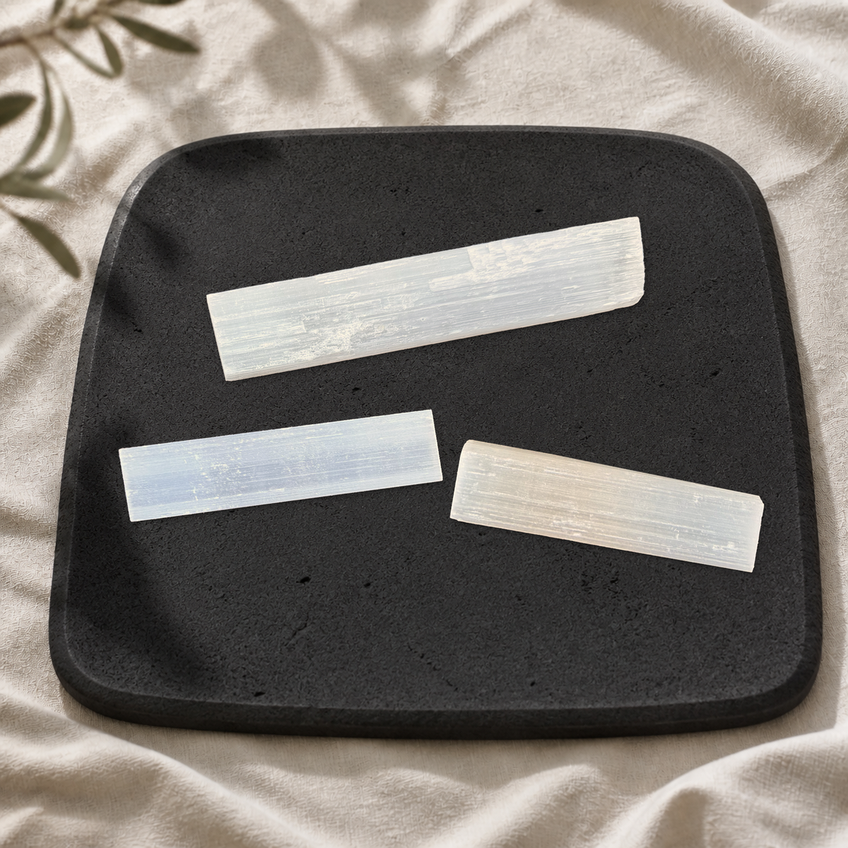 One long and two shorter white satin spar gypsum wands on a matte black limestone plate.