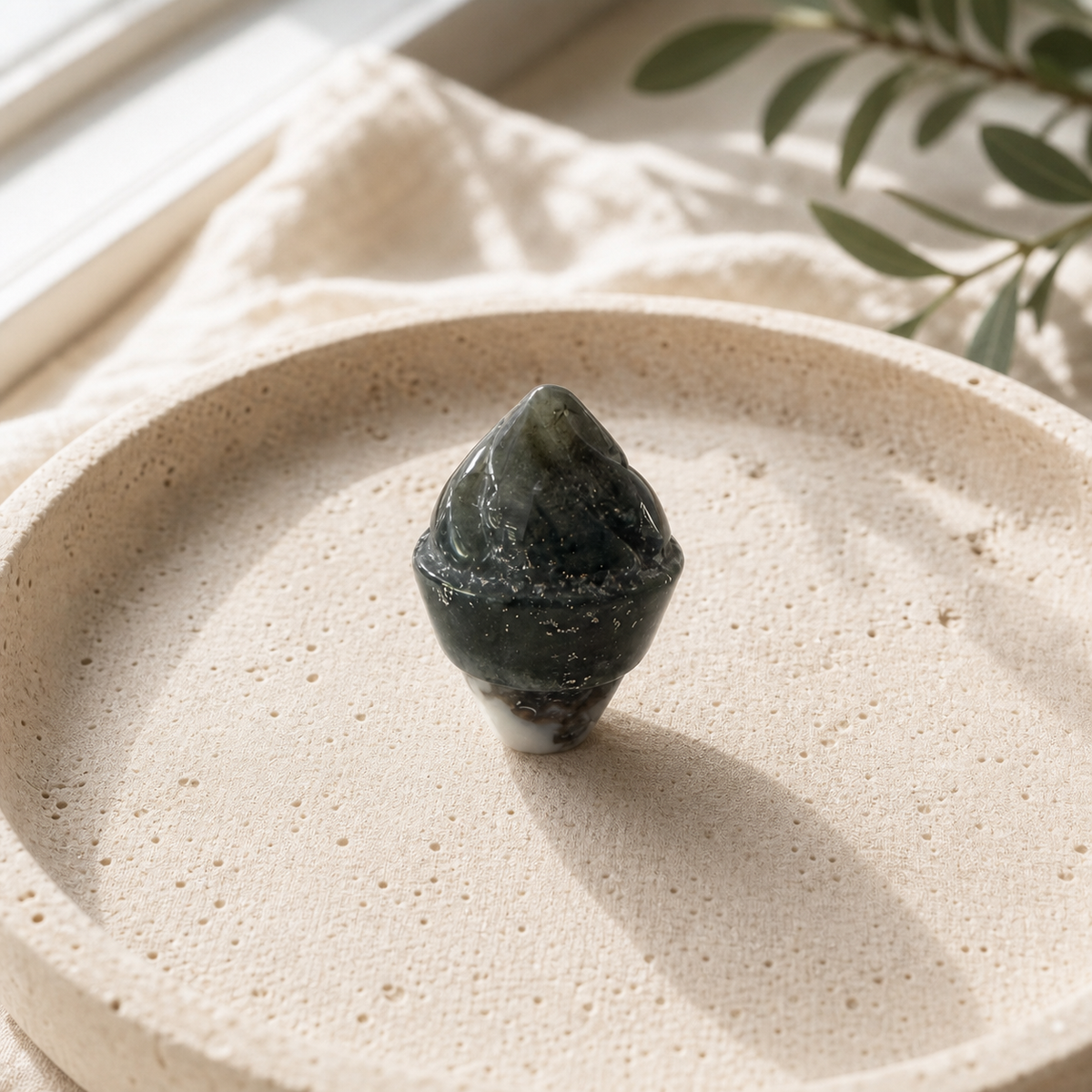 Green Moss Agate crystal ice-cream carving standing on a cream travertine plate