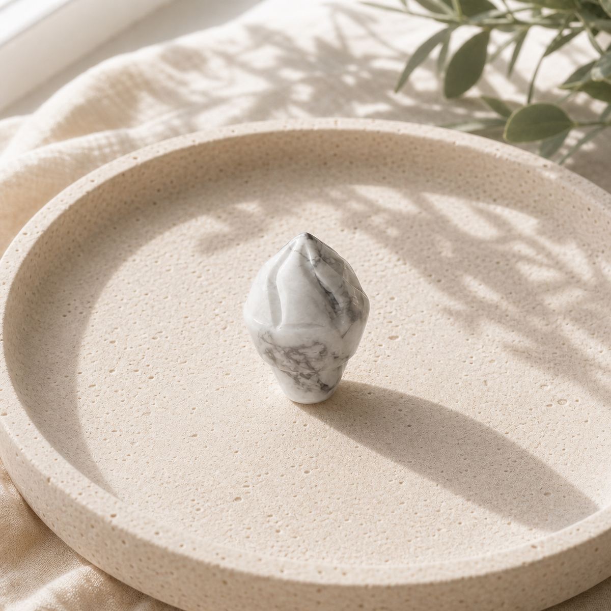 Howlite crystal ice-cream carving standing on a cream travertine plate