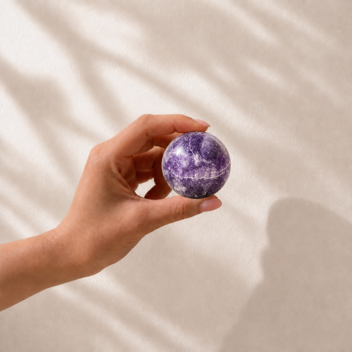 Hand holding a polished Lepidolite crystal sphere to show its approximate size