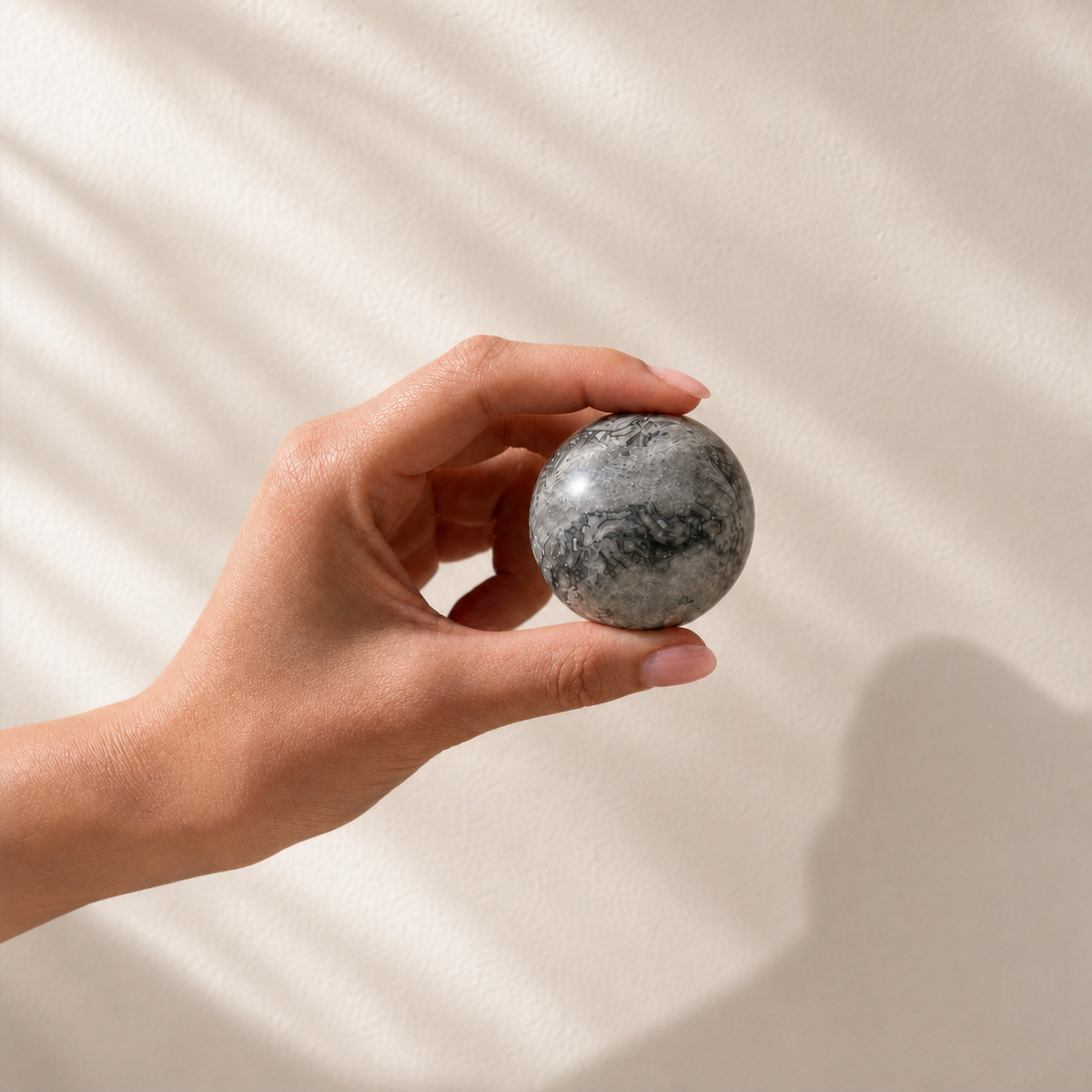 Picasso Jasper sphere held in hand against a warm wall to show its size and scale