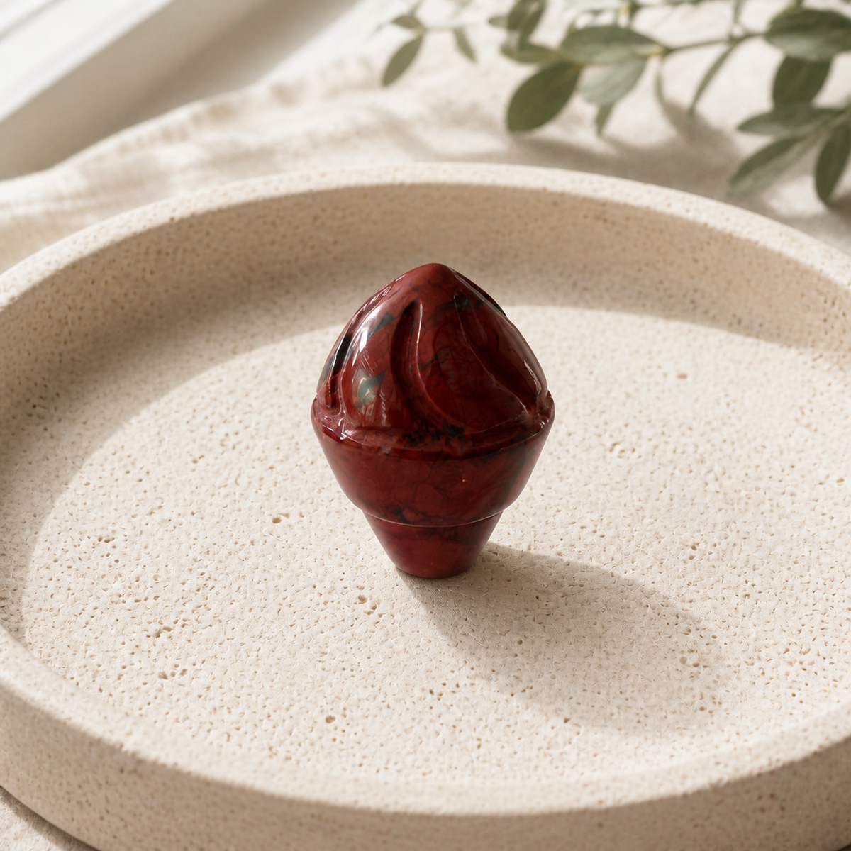 Red Jasper crystal ice-cream carving standing on a cream travertine plate