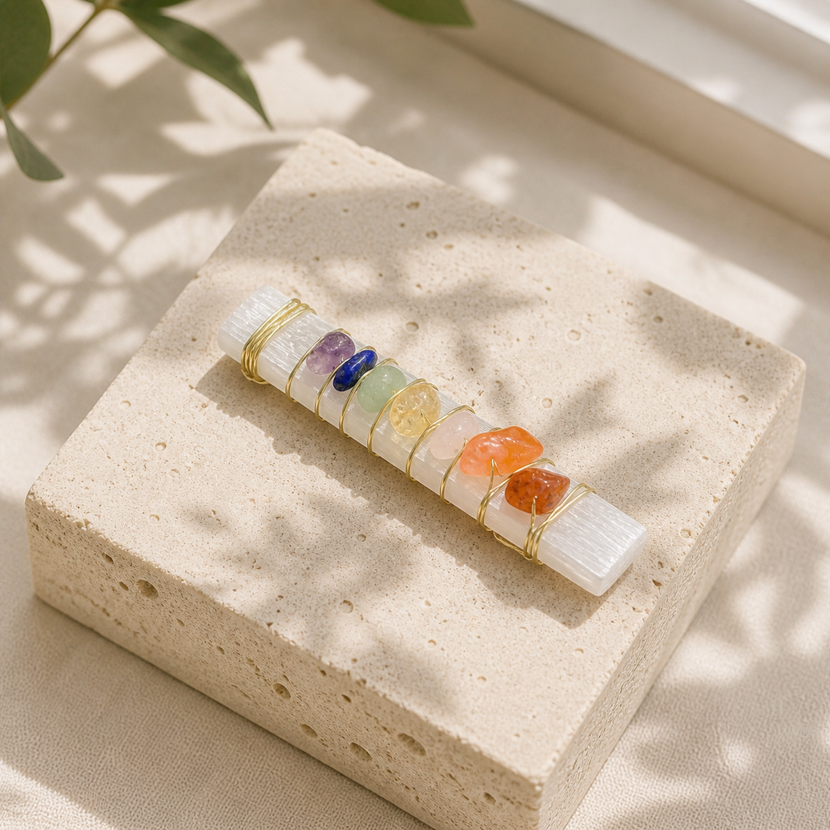 Selenite chakra cleansing wand with gold wire and crystal chips on a travertine block
