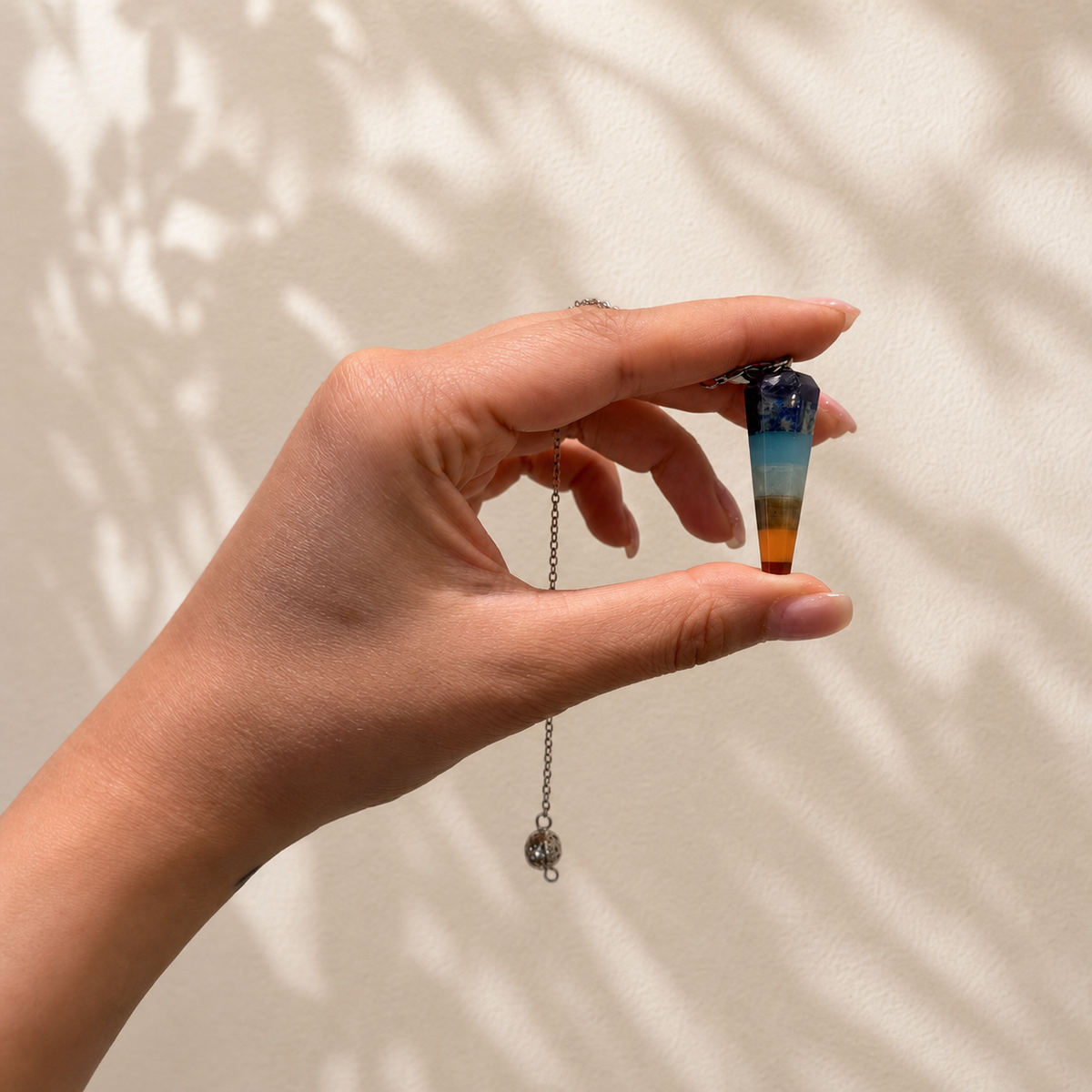 Seven chakra crystal pendulum held in hand for size reference