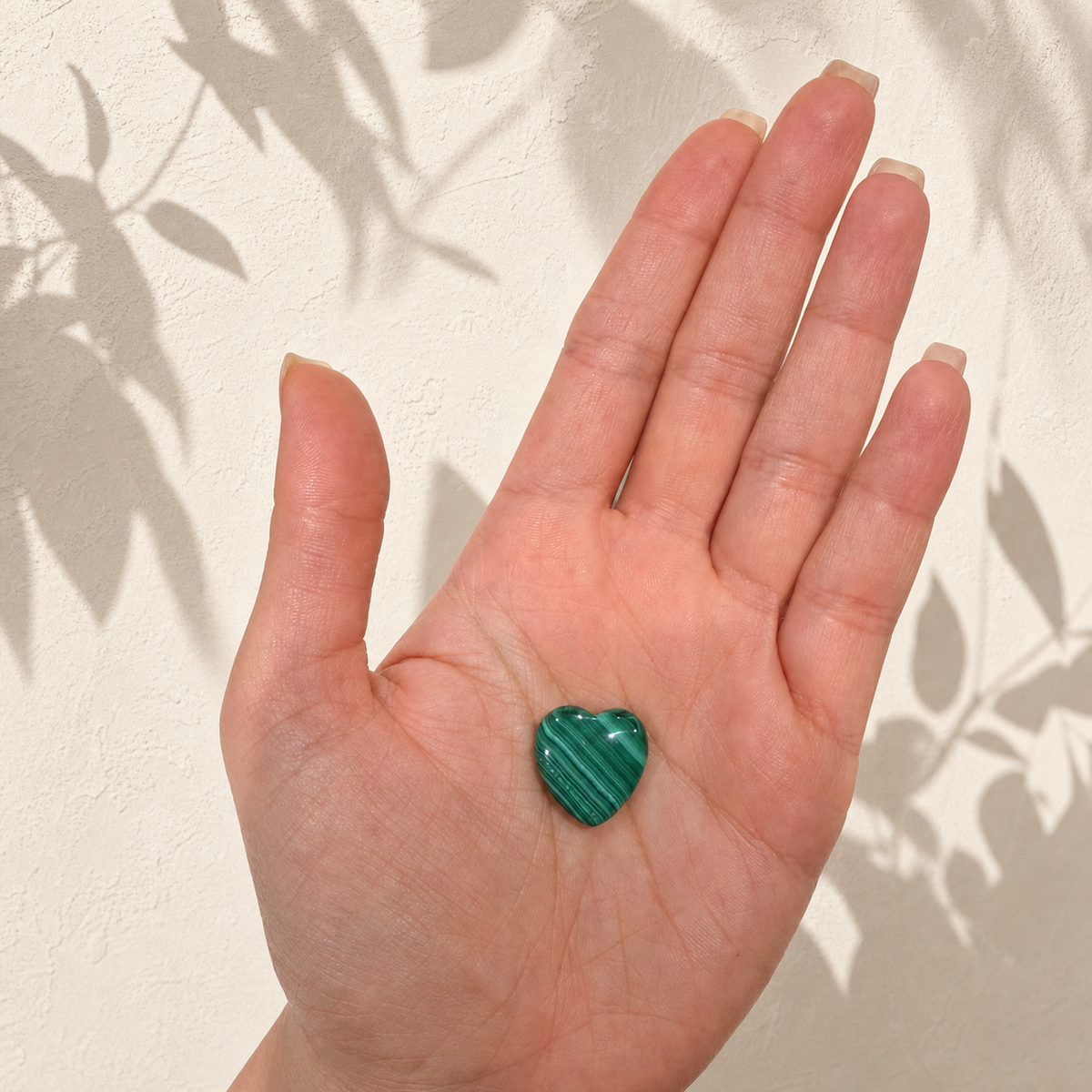 Small polished Malachite heart resting in a hand for size reference